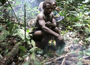 Baka, a Mbendjele pygmy, stops to make a fire in the northern forests of the Congo Republic, while another pygmy behind him holds a GPS handset
